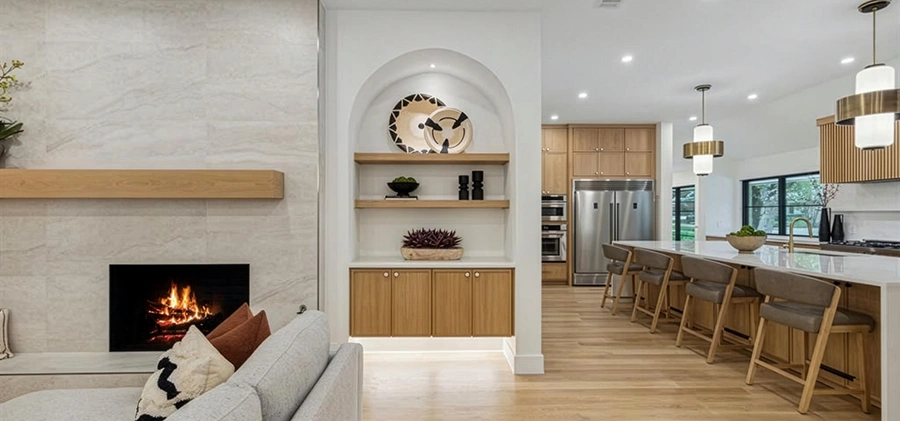 Detailed view of a staged kitchen island featuring a white waterfall countertop, light oak barstools with grey upholstered seats, modern white glass pendant lights, and an adjacent arched display alcove