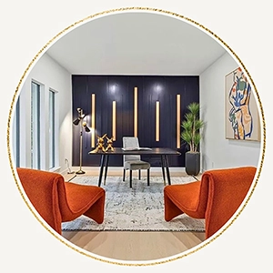 Circular image showcasing a staged home office featuring two vibrant burnt orange accent chairs in the foreground, a dark wood desk, and a bold navy blue accent wall with vertical wood slats