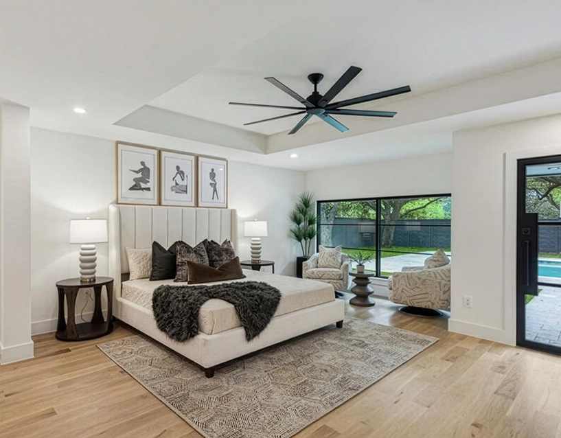 Staged primary bedroom showcasing a tall white vertical channel-tufted headboard, dark charcoal accent pillows, a plush faux-fur throw blanket, and an oversized black multi-blade ceiling fan
